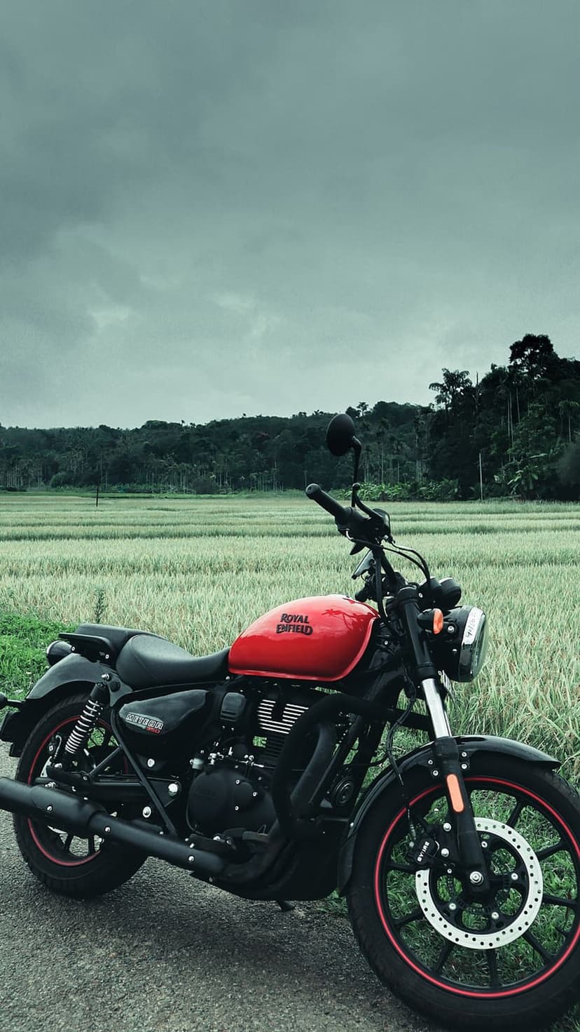 Royal Enfield Meteor 350 cruiser in red and black parked on a dirt trail beside a green rice paddy field.