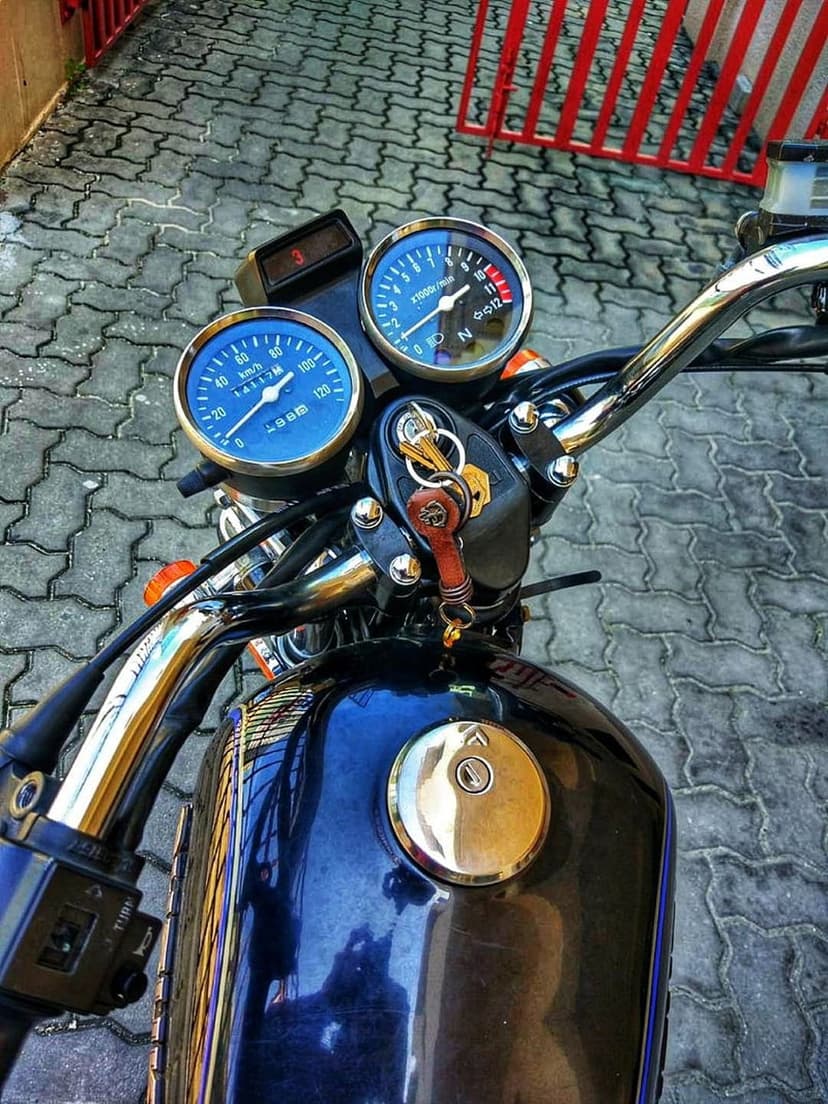 Blue motorcycle speedometer and tachometer set between chrome handlebars with an ignition key in the lock.