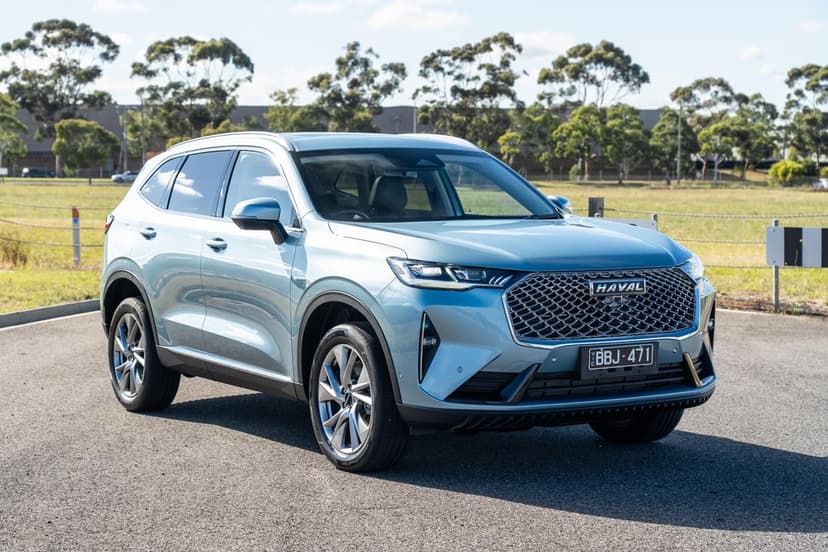 Metallic light blue Haval SUV parked on an asphalt lot with green trees and a bright blue sky in the background.