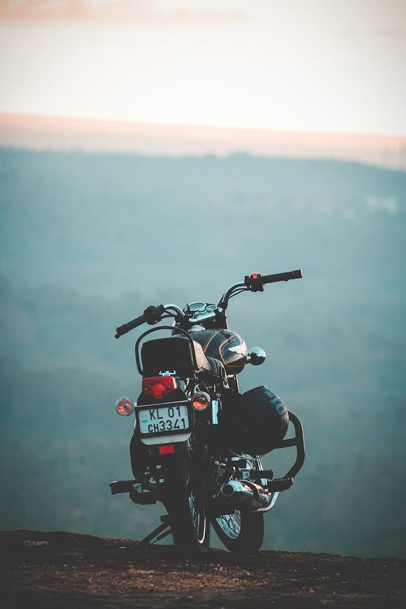 Black vintage motorcycle on a rocky cliff overlooking a misty mountain valley during a golden orange sunset.