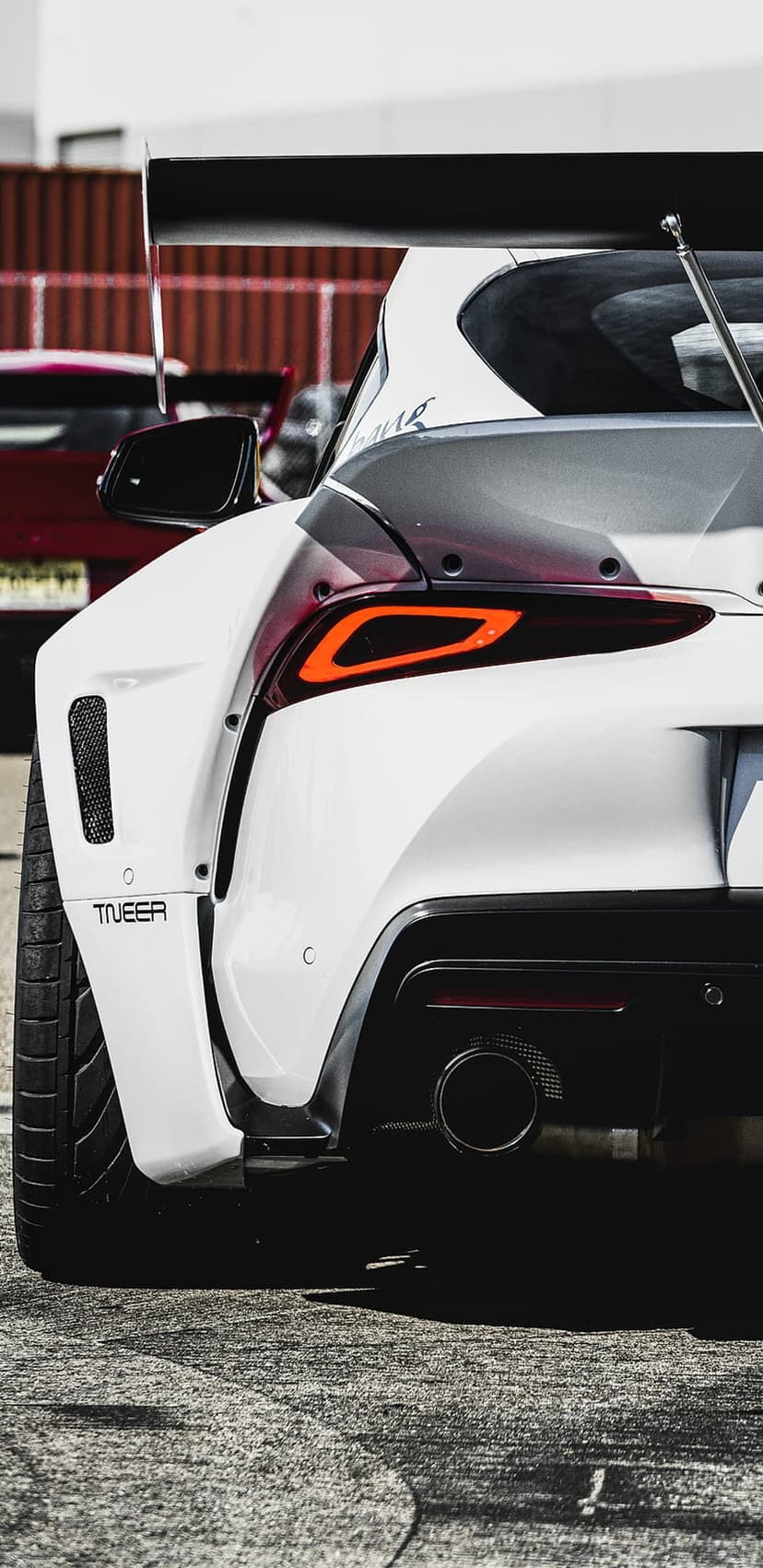 White Toyota Supra rear view featuring a large black spoiler, widebody fenders, and a custom oversized exhaust.