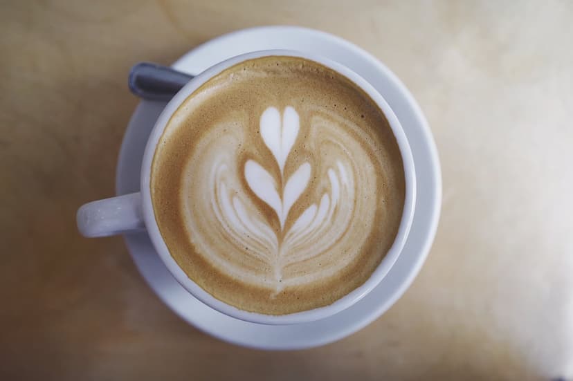 White ceramic cup filled with tulip latte art design on a saucer with a silver spoon under warm natural light.