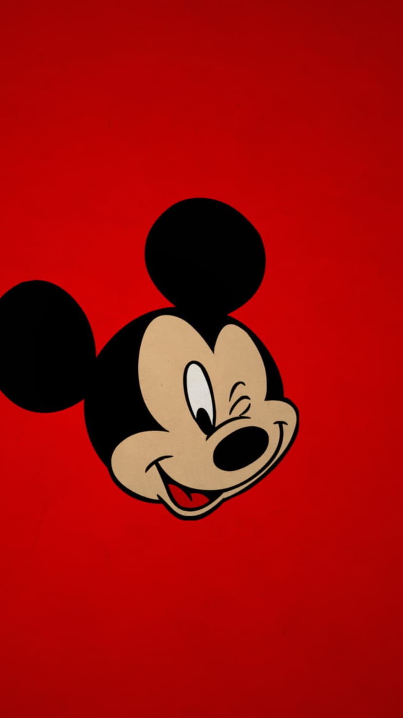 Mickey Mouse winking with one eye closed while smiling on a solid red background with his large black ears visible.