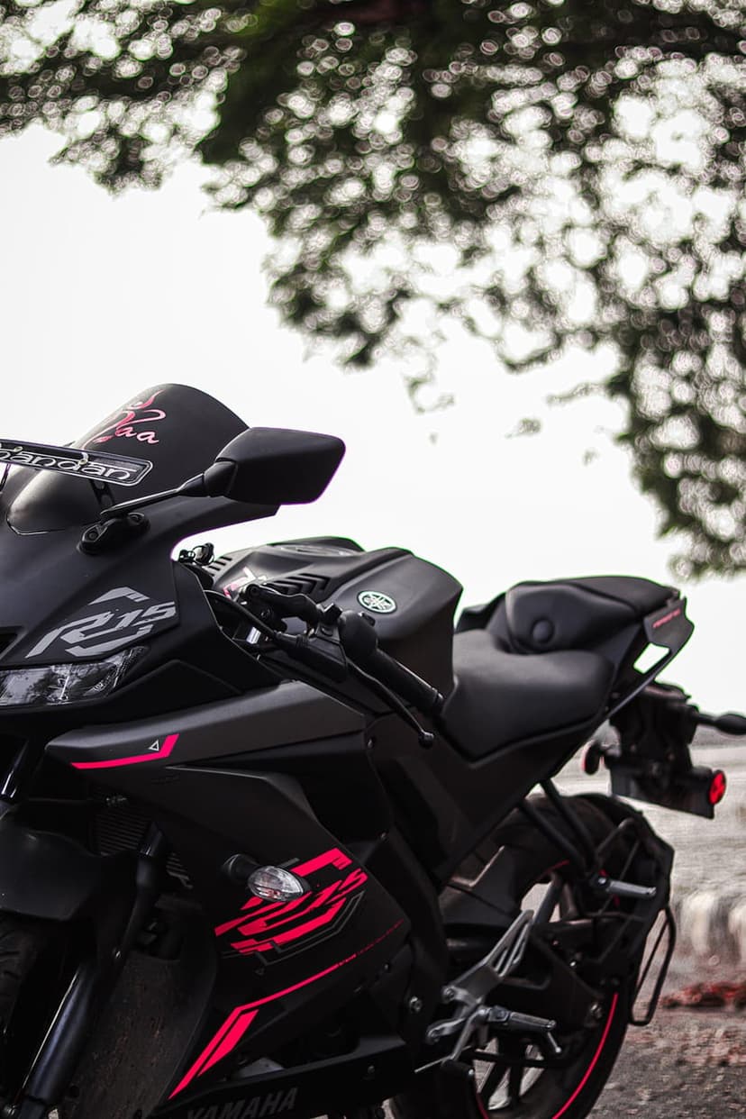 Yamaha R15 sportbike with pink stripes on a black fuel tank parked against a blurred background of green trees.