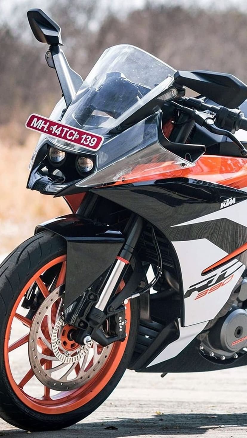 KTM RC 390 motorcycle front end featuring twin headlights, orange alloy wheels, and a black aerodynamic fairing.