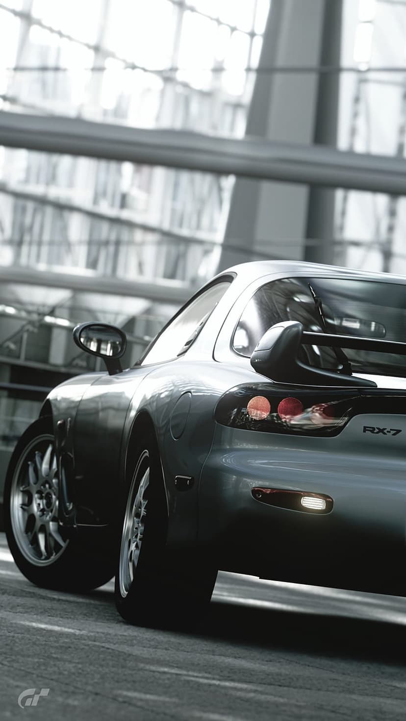 Mazda RX-7 rear view in silver paint features round taillights and a spoiler against a blurred city background.