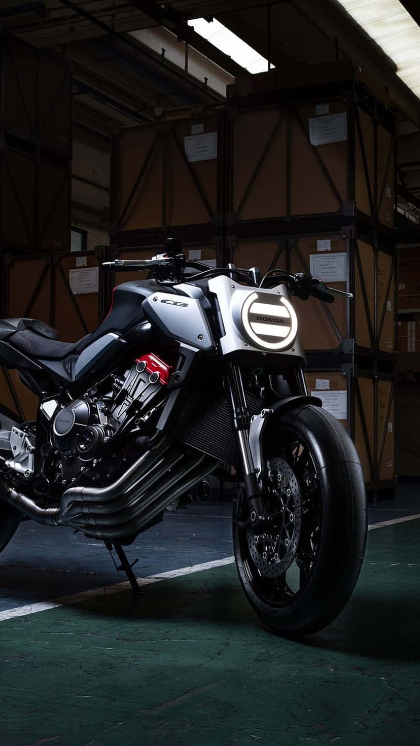Honda CB650R motorcycle with a lit LED headlight stands in a dark warehouse surrounded by cardboard crates.