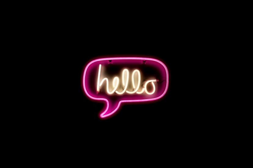 Neon pink speech bubble with a yellow cursive hello script glowing vividly against a dark black background.