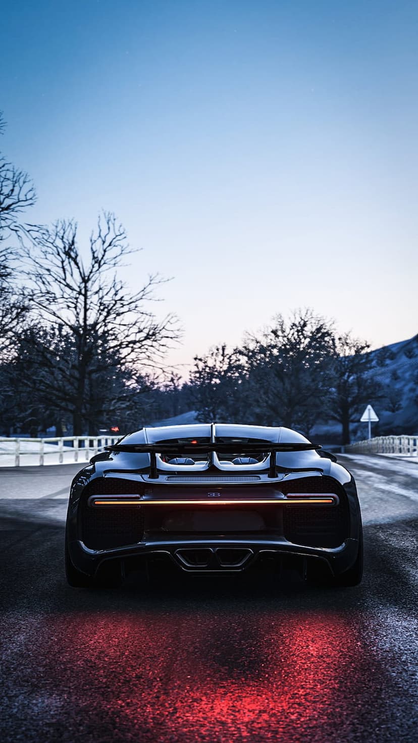 Bugatti Chiron rear light bar glowing orange on wet asphalt at dusk with bare trees in the dark background.