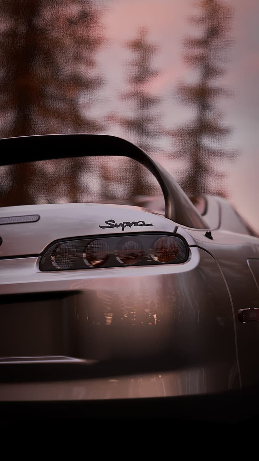 Toyota Supra taillights and rear wing spoiler on a silver car during a hazy sunset with blurred background trees.