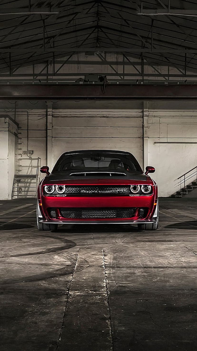 Red Dodge Challenger SRT Demon with glowing headlights parked on a concrete floor in a dark industrial warehouse.