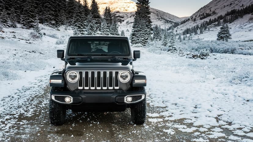 Black Jeep Wrangler parked on a snow-covered dirt road with pine trees and snowy mountains in the background.