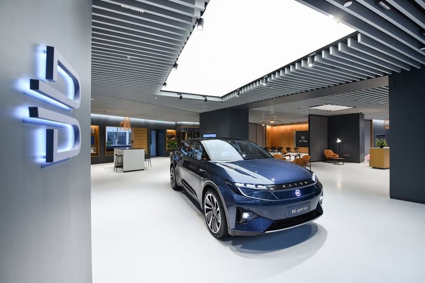 Navy blue Byton M-Byte electric car in a minimalist showroom with glowing blue logos and slatted ceilings.