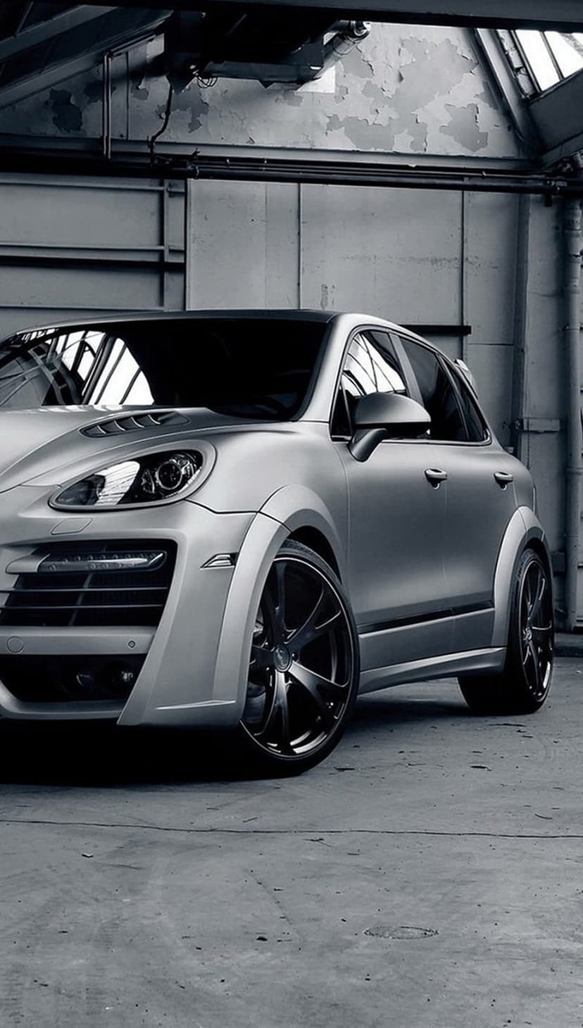 Silver Porsche Cayenne SUV with custom black wheels parked inside a dimly lit industrial warehouse setting.
