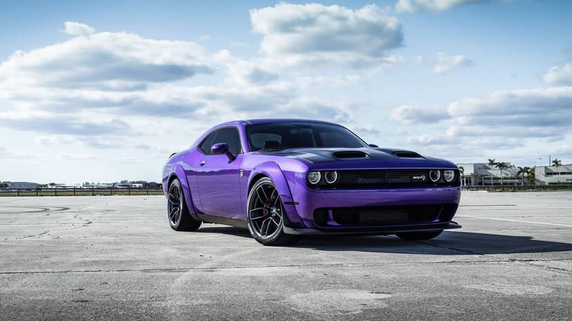 Purple Dodge Challenger SRT Hellcat Widebody with black hood on concrete under a blue cloudy sky.