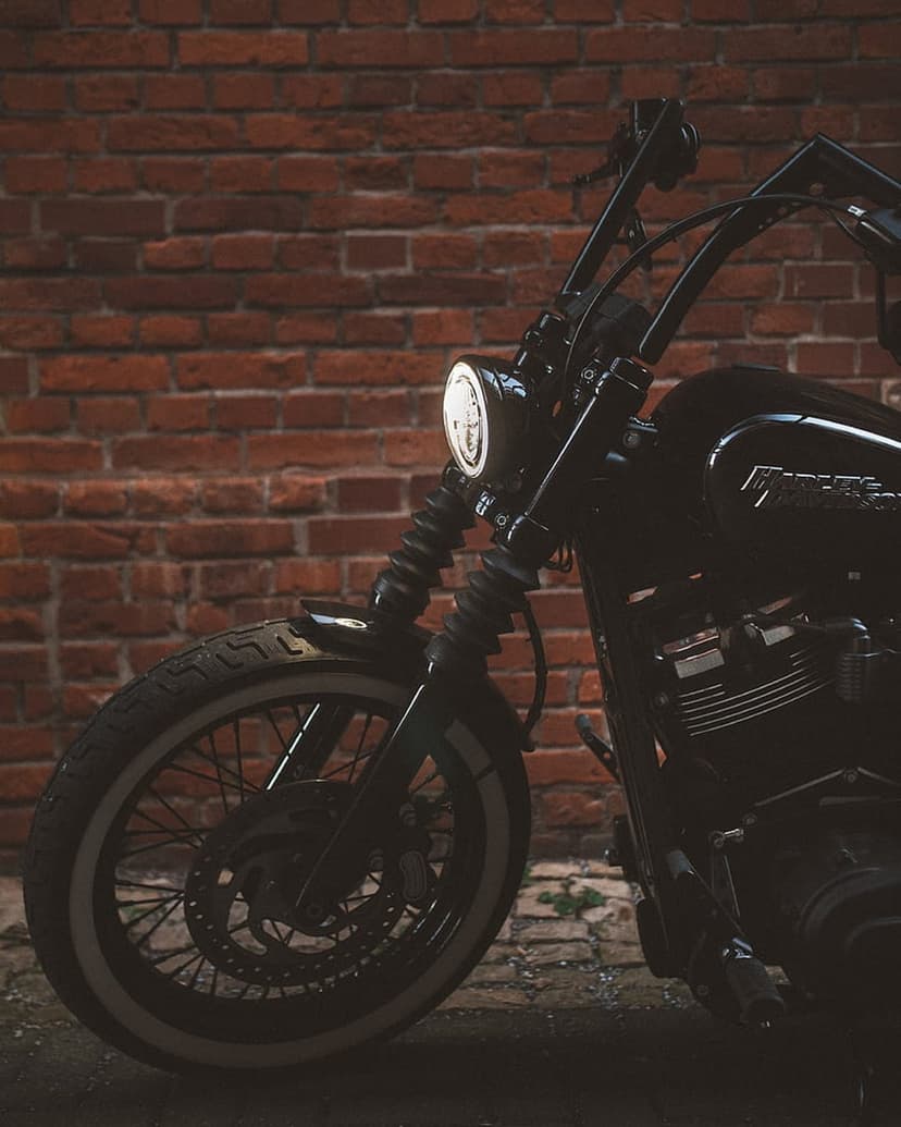 Black Harley Davidson motorcycle front wheel and chrome engine parked against a textured red brick wall.