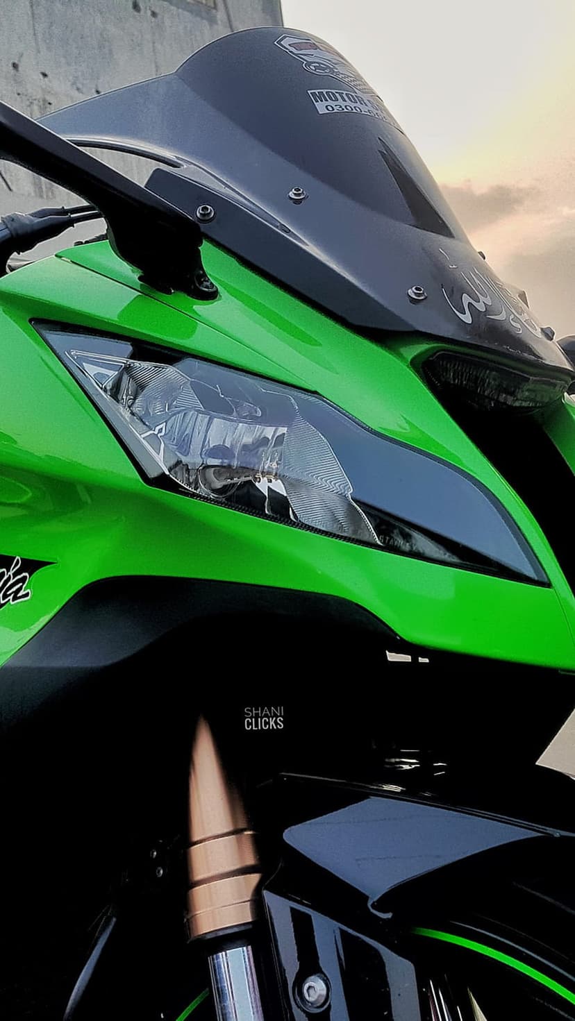 Green sportbike front fairing and glass headlight with aerodynamic lines against a blurred neutral backdrop.
