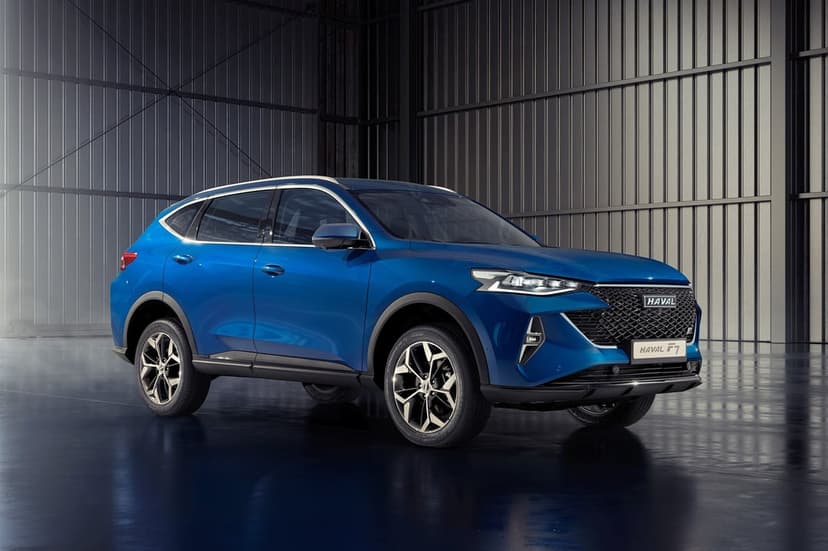 Blue Haval F7 SUV parked in a dark industrial hangar with corrugated walls and a reflective floor.