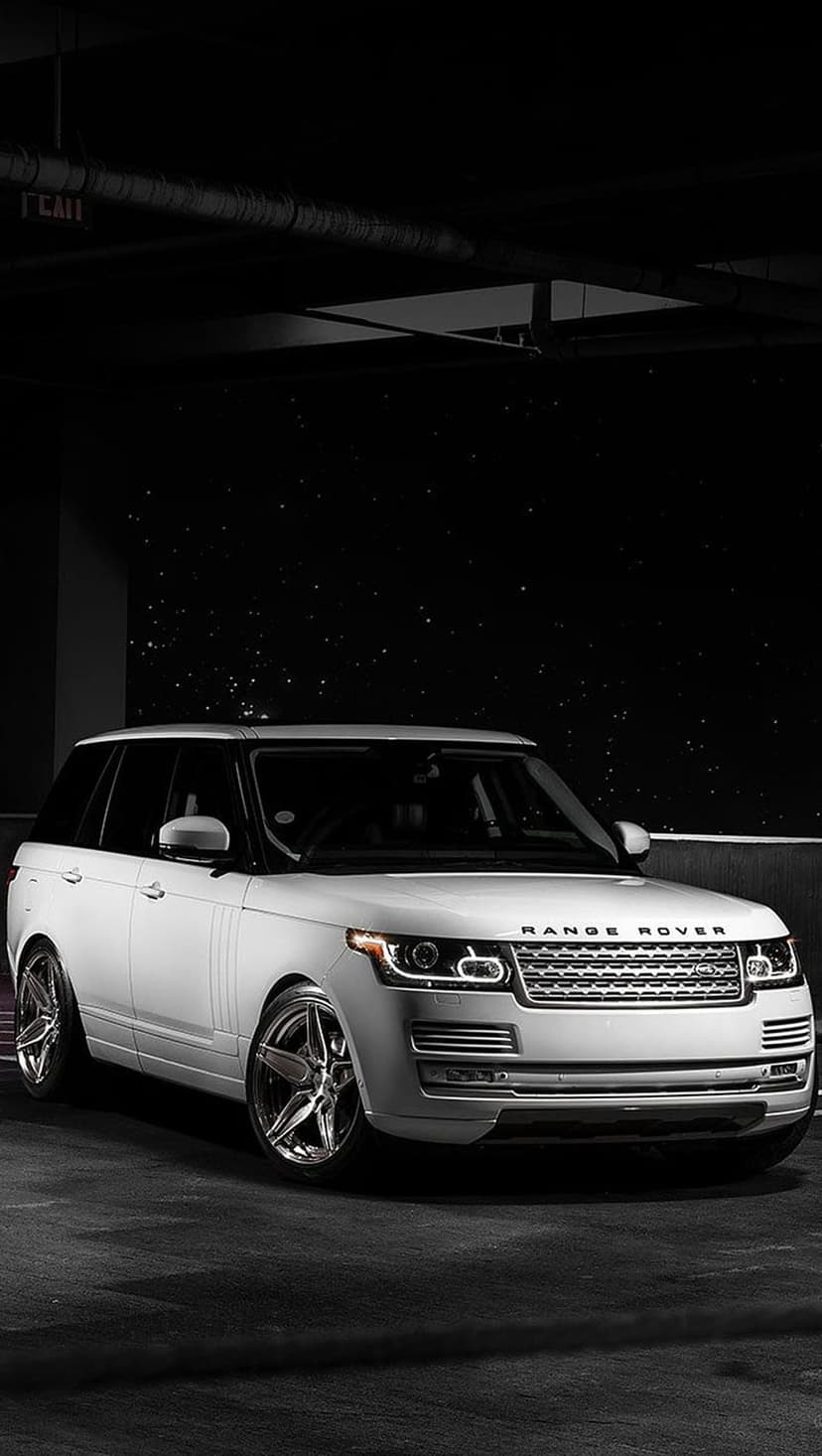 White Range Rover with a honeycomb grille and alloy wheels parked inside a dark industrial garage with shadows.