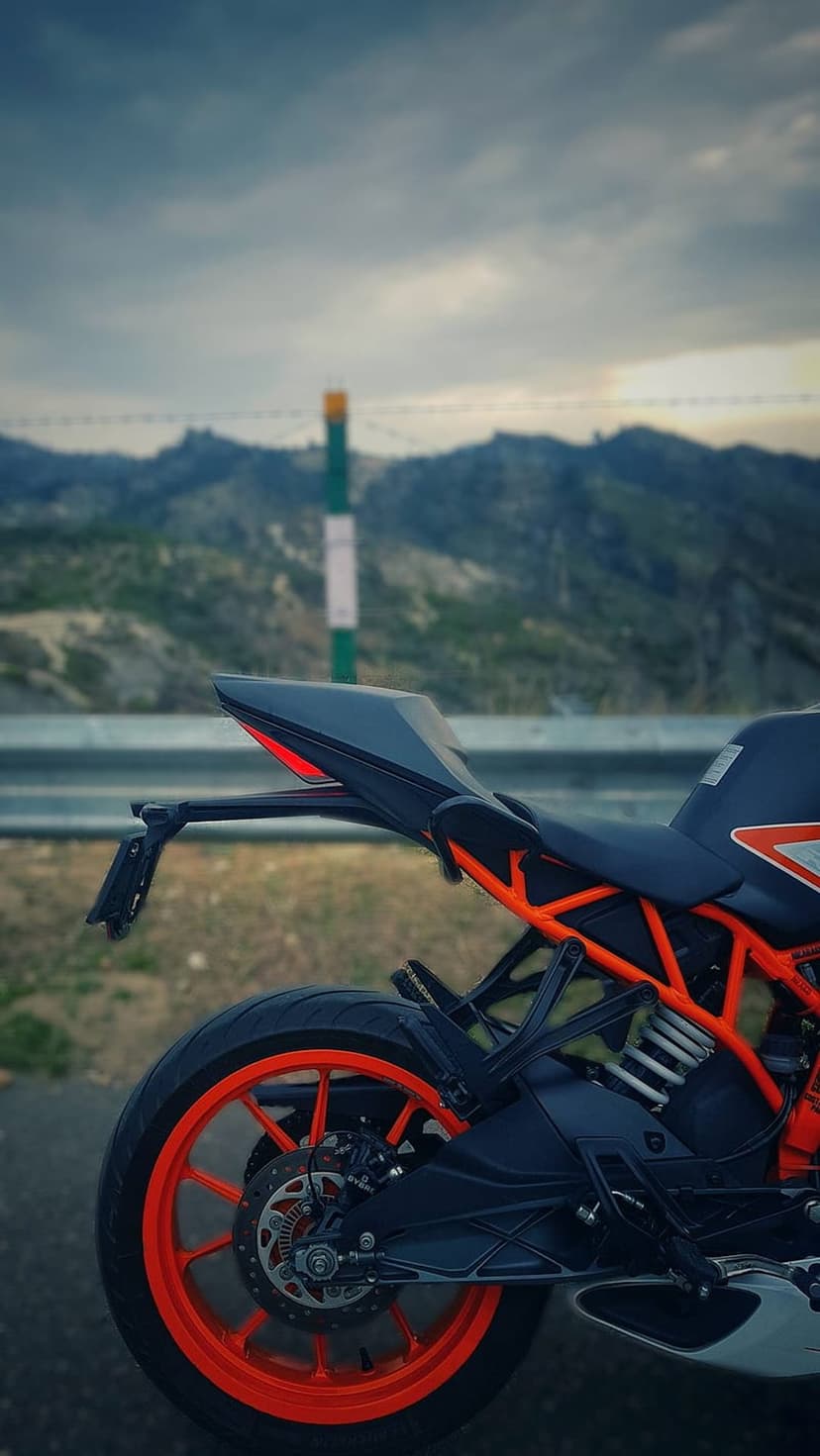 KTM motorcycle with an orange frame parked on a mountain roadside under a stormy sky with rolling green hills.