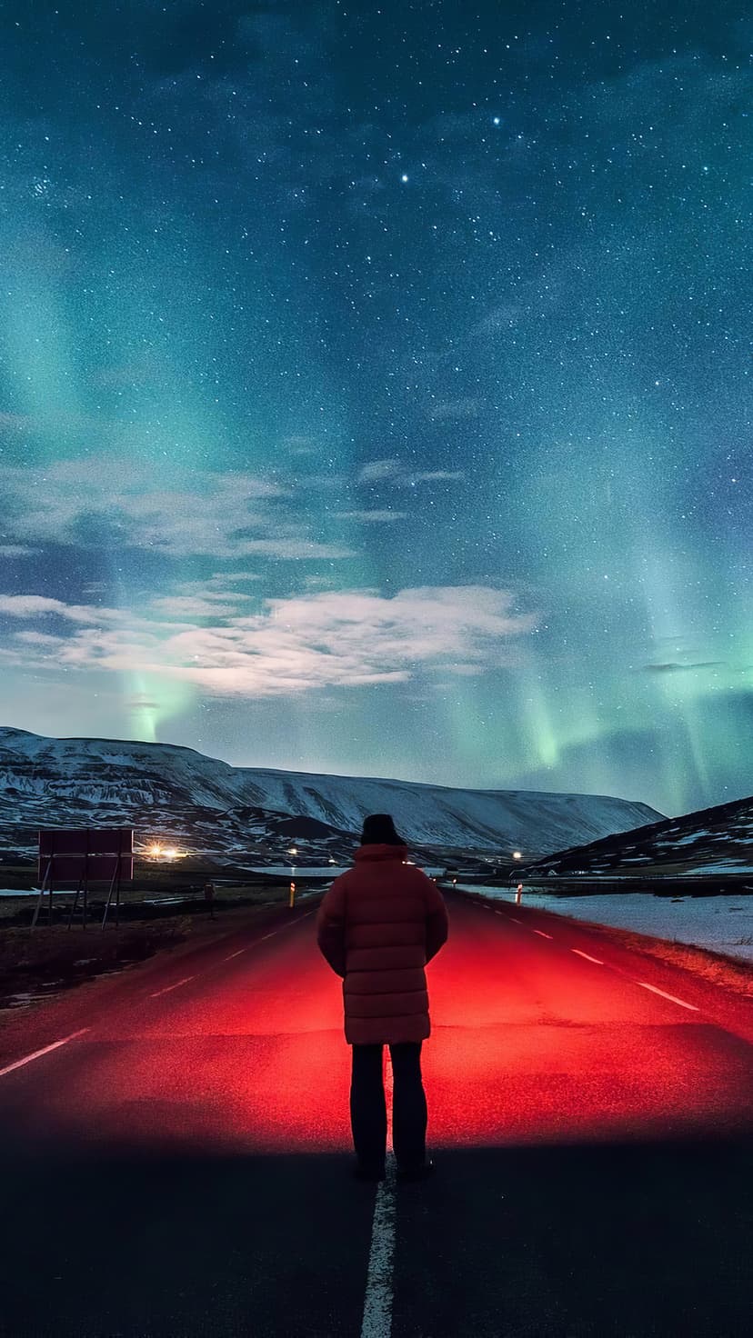 Solitary person on a road stands under a green aurora borealis and starry sky with a bright red light source.