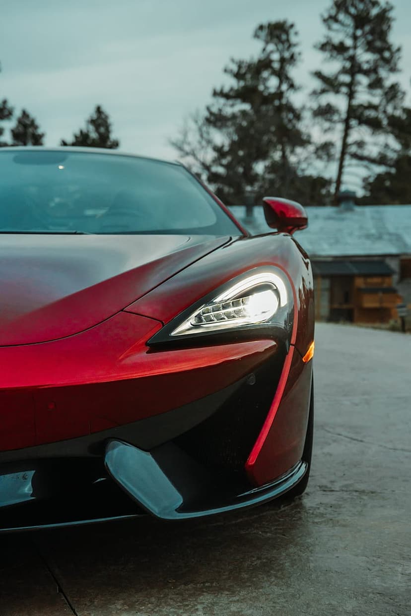 Red McLaren supercar front view with illuminated headlights on a scenic rural road under soft lighting.