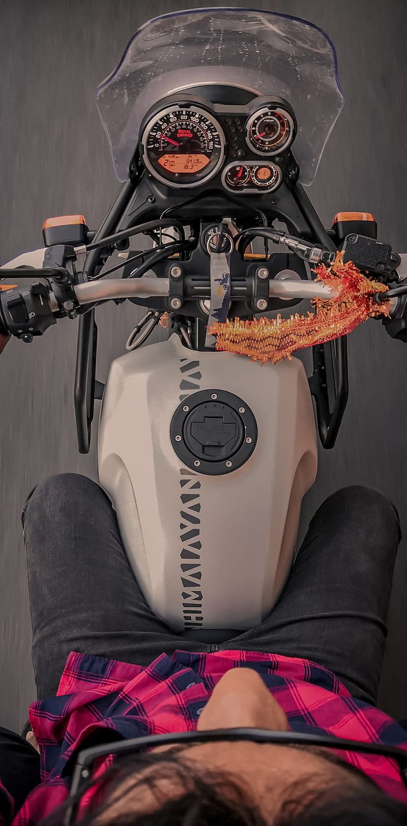 Royal Enfield Himalayan handlebars and white fuel tank seen from a biker's point of view wearing a plaid shirt.