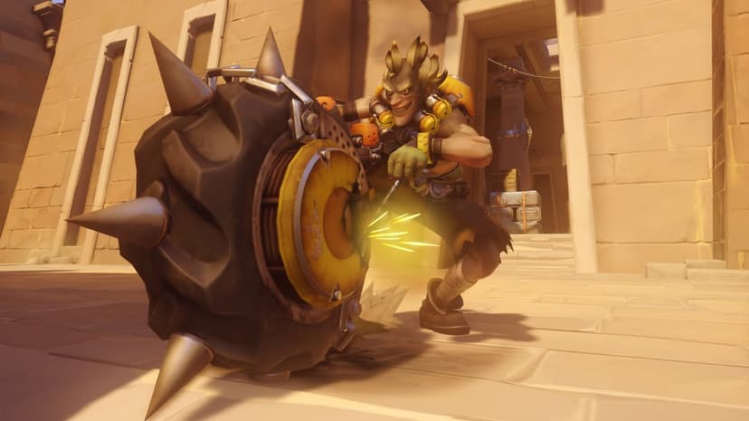 Junkrat crouches by a large spiked tire with yellow sparks flying in a sunlit desert temple setting.