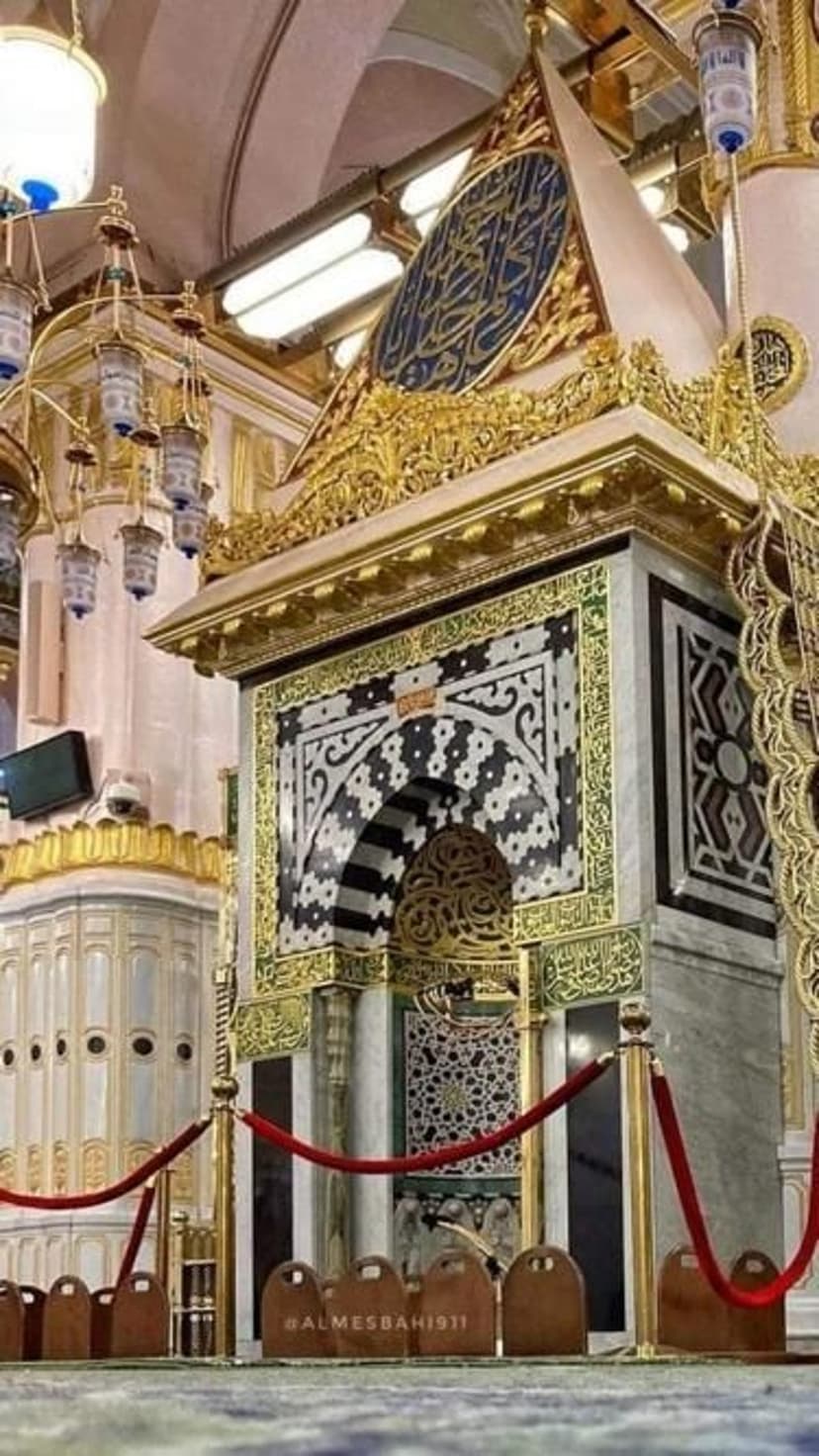Golden Islamic calligraphy and geometric patterns on a mosque wall with hanging lamps in a vertical view.