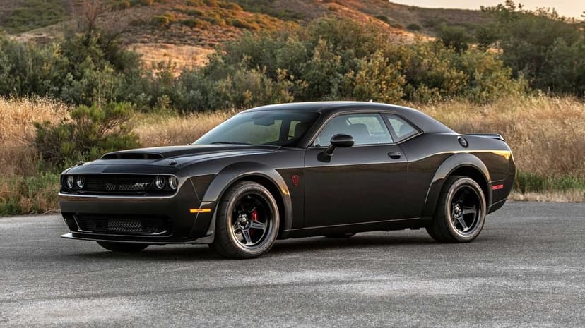 Black Dodge Challenger SRT Demon muscle car parked on a road with hilly landscape during sunset lighting.