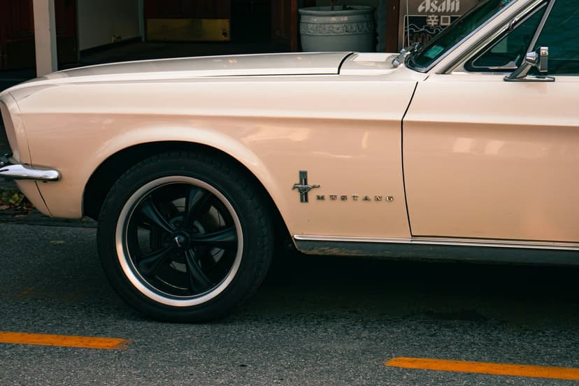 Vintage Ford Mustang fender with a chrome pony badge and black alloy wheel parked over yellow road lines.