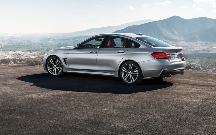 Silver BMW 4 Series Gran Coupe parked on a high overlook with a vast mountain valley background in daylight.