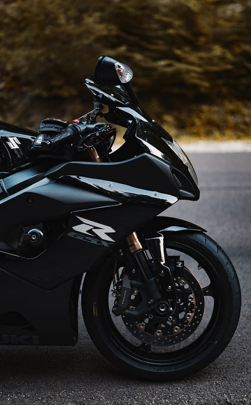 Suzuki GSX-R motorcycle with glossy black fairings and disc brakes parked on a road with a blurred hillside.