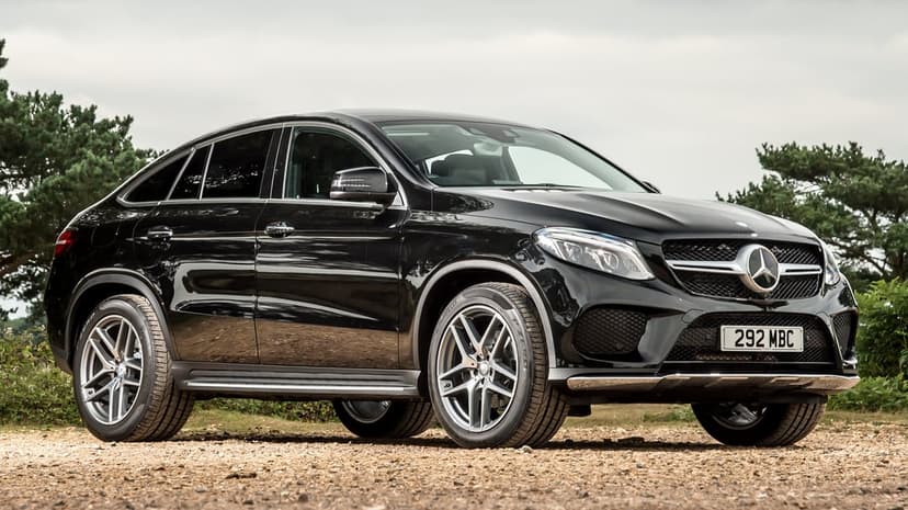Black Mercedes-Benz GLE Coupe SUV on gravel with trees and an overcast sky in a professional car portrait.