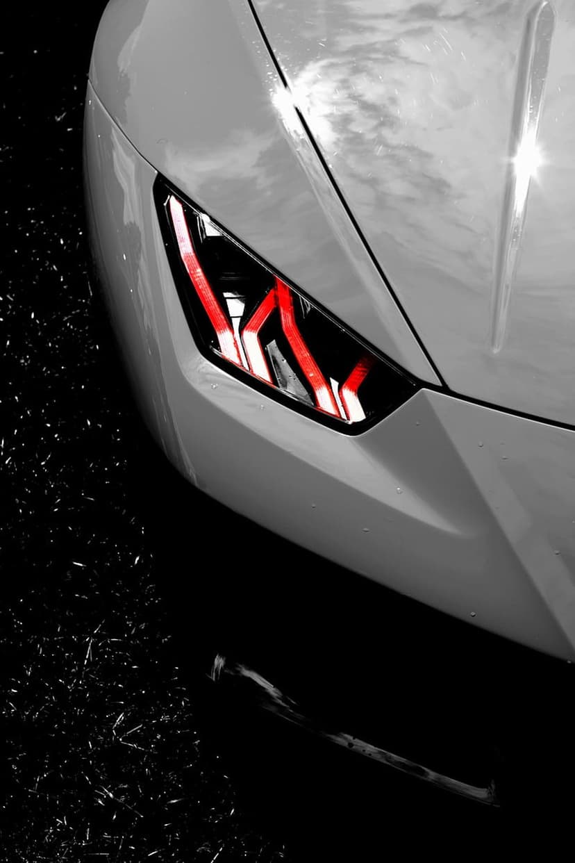 White car headlight with glowing red internal LEDs and scattered water droplets on the metallic exterior surface.