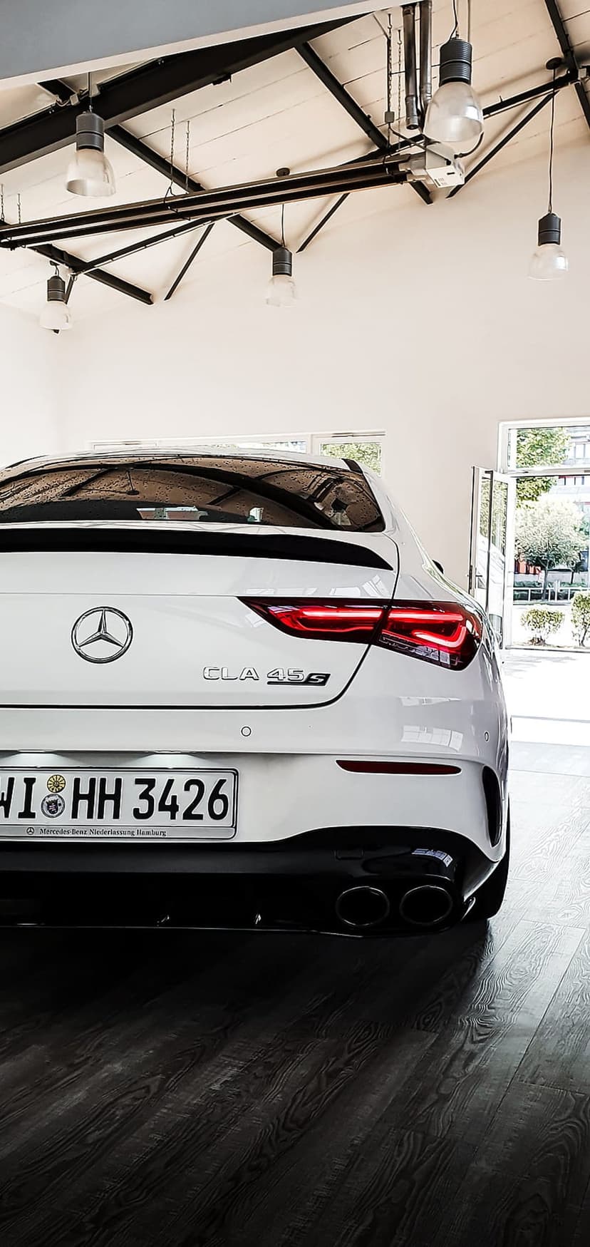 Mercedes-Benz CLA 45 S rear view with glowing LED taillights and quad exhausts on a polished dark wood floor.