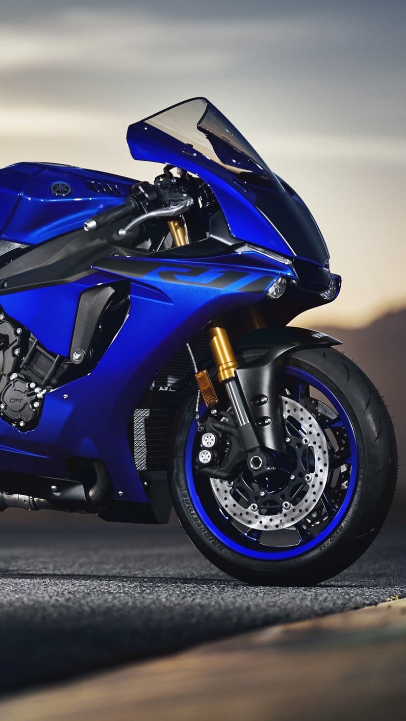 Blue Yamaha R1 motorcycle with gold front forks and dual disc brakes parked on a paved road at dusk.