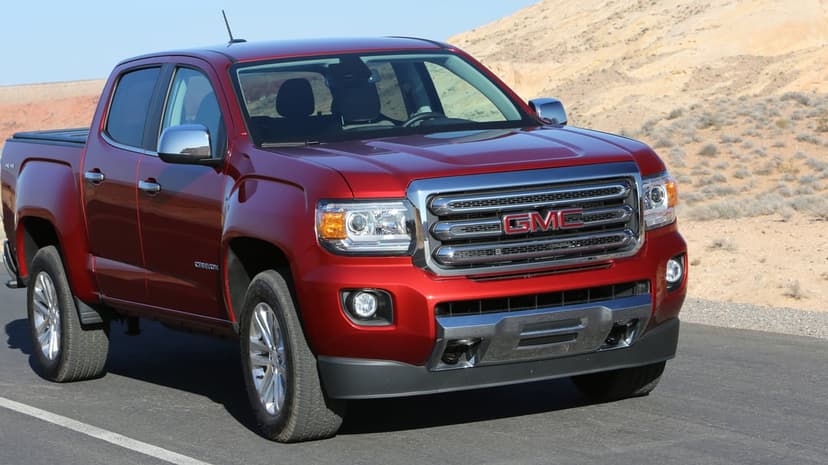 Metallic red GMC Canyon truck on an asphalt road with tan desert hills and a blue sky in the background.