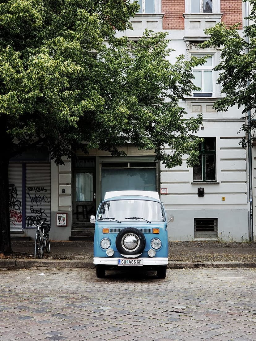 Blue vintage camper van with a front spare tire parked on a cobblestone street beside a bicycle and graffiti.