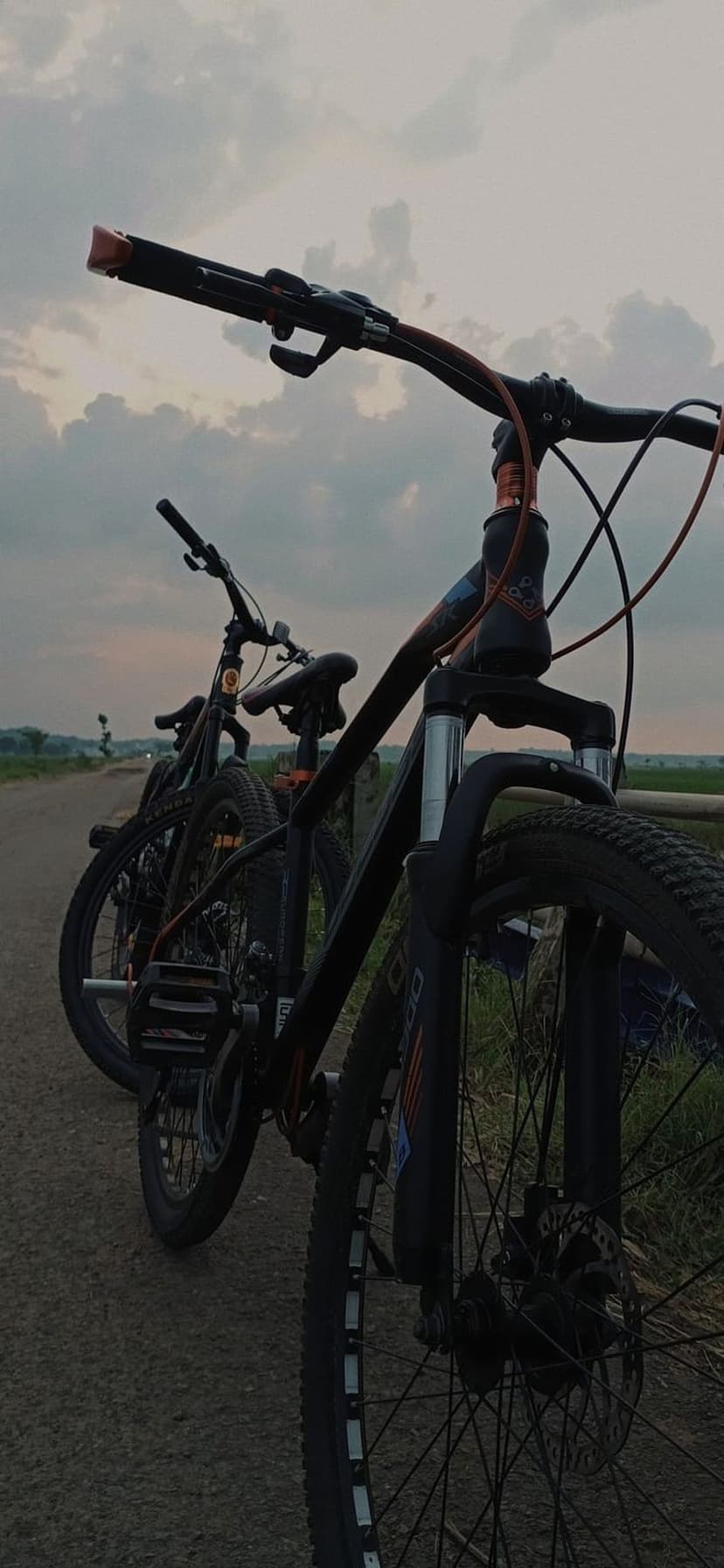 Two black mountain bikes parked on a dirt road during a vibrant sunset with dramatic orange-lit clouds.