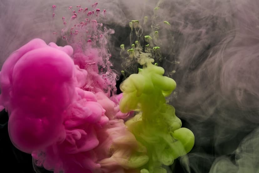 Magenta and lime green ink plumes swirl in dark water with tiny droplets and delicate, wispy fluid tendrils.