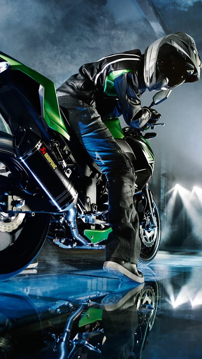 Motorcyclist in full gear on a lime green sportbike with a carbon exhaust pipe on a reflective wet floor.