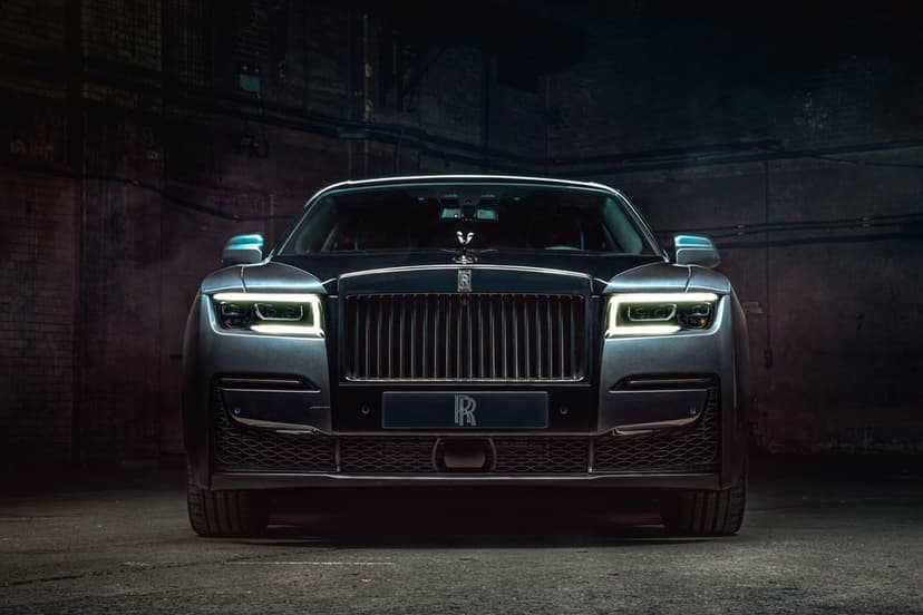 Front view of a dark grey Rolls-Royce Ghost with glowing LED headlights in a dim industrial garage background.