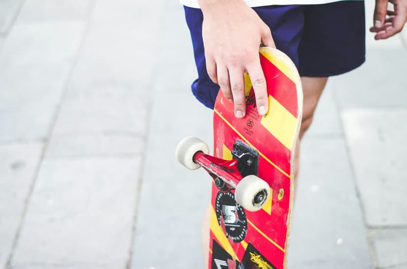 Skateboarder holds a red and yellow striped skateboard with white wheels against a blurred pavement background.