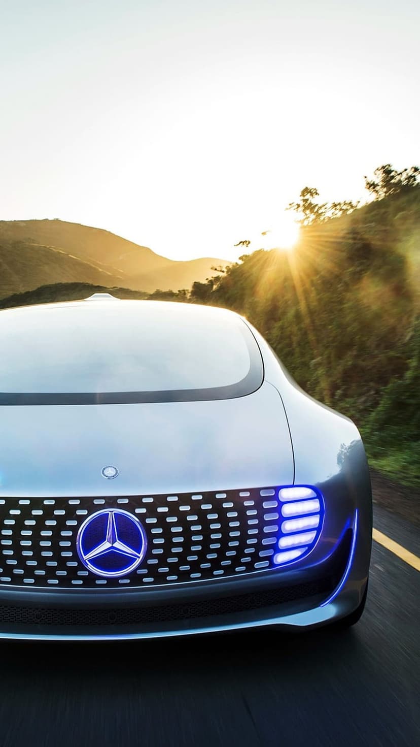 Mercedes-Benz concept car with glowing blue LED lights driving on a winding road during a vibrant sunset.