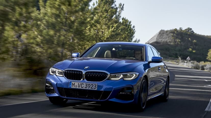 Blue luxury sedan driving on a curved road with motion blur and green pine trees in the background.