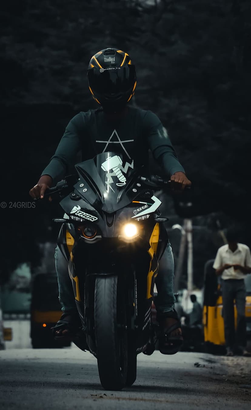 Motorcyclist in a yellow-accented helmet riding a sportbike at dusk with a bright headlight on a dark road.