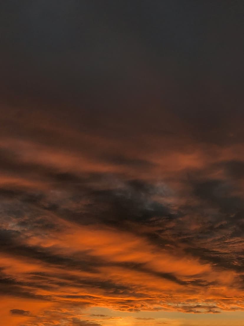 Fiery orange and dark gray clouds spread across a vertical twilight sky with intense golden light highlights.