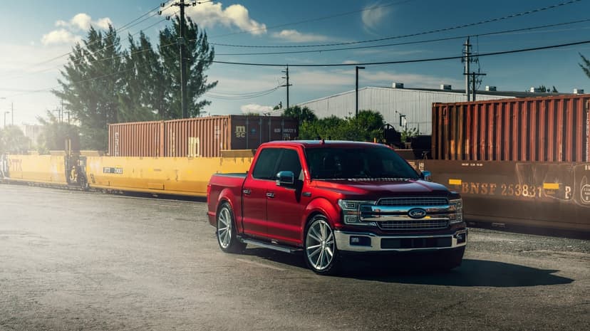 Red Ford F-150 truck with custom wheels parked next to industrial shipping containers under a sunny blue sky.