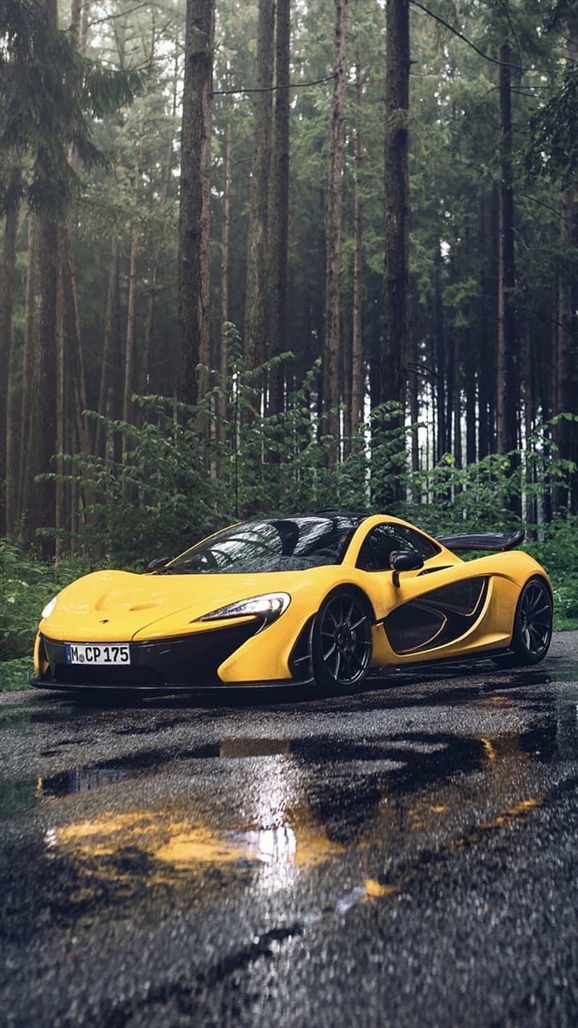 Yellow McLaren P1 supercar parked on wet forest asphalt with rain reflections for a mobile phone background.